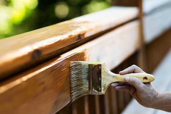 Cropped view of male carpenter applying stain to wooden furniture. Horizontal shot.